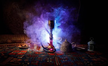 Hookah hot coals on shisha bowl making clouds of steam at Arabian interior. Oriental ornament on the carpet eastern tea ceremony. Stylish oriental shisha in dark with backlight. Selective focus clipart