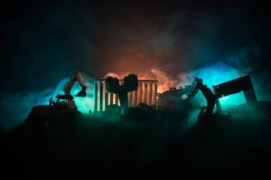 Şehir caddesinde bir inşaat alanı. Gece boyunca inşaat alanında park etmiş sarı kazıcı kazıcısı. Karanlık sisli arka planda endüstriyel konsept masa dekorasyonu. Seçici odak