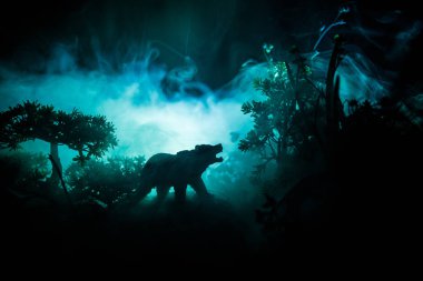 Horror view of big bear in forest at night. Angry bear behind the fire cloudy sky. The silhouette of a bear in foggy forest dark background clipart