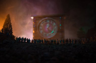 Büyük bir kalabalığa karşı bir tonda ışık ışınları sisli arka plan üzerinde büyük ok saatiyle gece ayakta, ormandaki insan silüeti. Zaman kavramı. Kum saati geçen süre ölçümünü