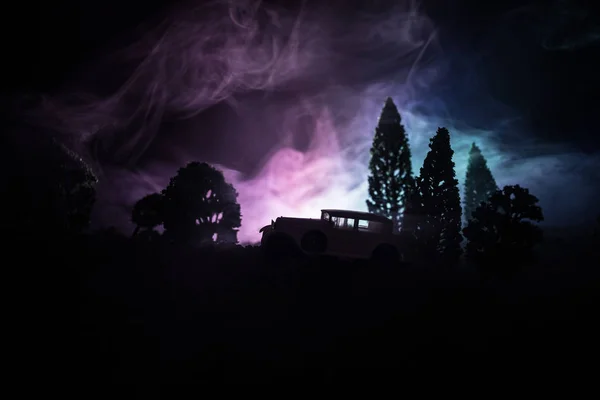 Silhouette of old vintage car in dark foggy toned background with glowing lights in low light, or silhouette of old car in dark forest. Selective focus