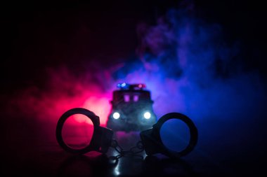 Polis baskını gece ve sen altında tutuklama kavramı vardır. Kelepçe arka polis araba ile silüeti. Görüntü yanıp sönen kırmızı ve mavi polis ışıklardan sisli arka plan ile. Kaymak vurdu