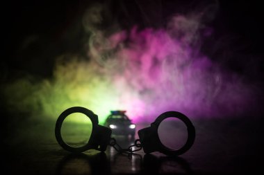 Polis baskını gece ve sen altında tutuklama kavramı vardır. Kelepçe arka polis araba ile silüeti. Görüntü yanıp sönen kırmızı ve mavi polis ışıklardan sisli arka plan ile. Kaymak vurdu