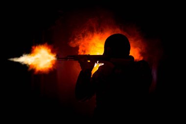 Saldırı tüfeği koyu tonda sisli arka plan veya siyah yün ve holding silahı elinde giyen tehlikeli bir haydut saldırmaya hazır olan adam silüeti. Terörist silah Tema dekor ile çekim