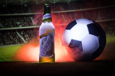Bakü, Azerbaycan - 15 Haziran 2018: Yaratıcı kavramı. Futbol topu ve bulanık Stadyumu ateşi bulutlar ile arka plan üzerinde çim Tuborg cam şişe bira. Tuborg Kuzey banliyösü olan Kopenhag, Danimarka