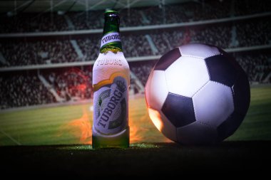 Bakü, Azerbaycan - 15 Haziran 2018: Yaratıcı kavramı. Futbol topu ve bulanık Stadyumu ateşi bulutlar ile arka plan üzerinde çim Tuborg cam şişe bira. Tuborg Kuzey banliyösü olan Kopenhag, Danimarka