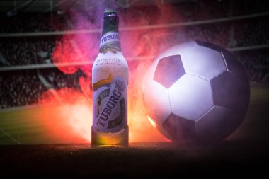 Bakü, Azerbaycan - 15 Haziran 2018: Yaratıcı kavramı. Futbol topu ve bulanık Stadyumu ateşi bulutlar ile arka plan üzerinde çim Tuborg cam şişe bira. Tuborg Kuzey banliyösü olan Kopenhag, Danimarka
