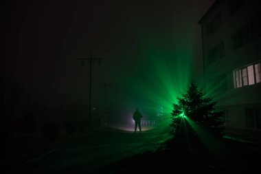 Gece manzarası. Gece yoğun sis içinde şehir. Mistik manzara ürkütücü adam gerçeküstü ışıklarla. Yapay ışıkta gece siste yürüyen adamın siluet. Arka aydınlatma karışık güzel.