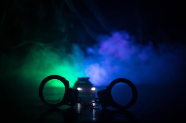 Polis baskını gece ve sen altında tutuklama kavramı vardır. Kelepçe arka polis araba ile silüeti. Görüntü yanıp sönen kırmızı ve mavi polis ışıklardan sisli arka plan ile. Kaymak vurdu