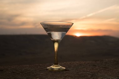 Dağları ile günbatımı arka plan karşı bir bardak Martini. İçki günbatımı zaman kulübü. Seçici odak