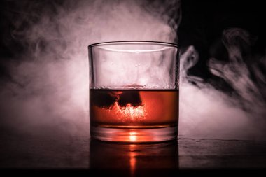 Bardak viski ve buz ile renk ışık ahşap yüzeyde ve sis arka plan üzerinde. Yakın çekim. Reklam atış