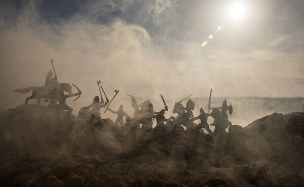 Medieval battle scene with cavalry and infantry. Silhouettes of figures as separate objects, fight between warriors on sunset foggy background. Selective focus