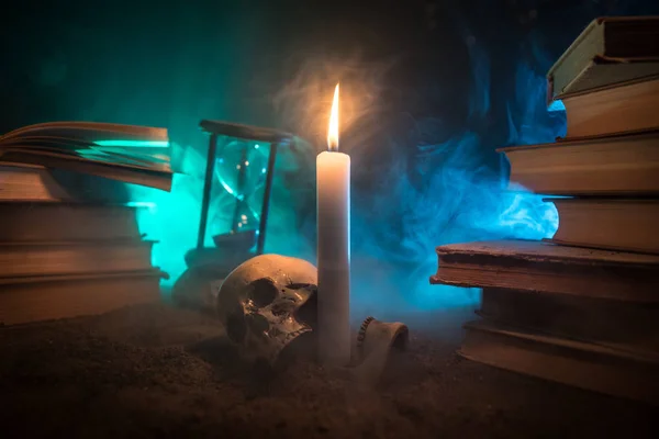Wizard\'s Desk. A desk lit by candle light. A human skull, old books on sand surface. Halloween still-life background with a different elements on dark toned foggy background. Selective focus