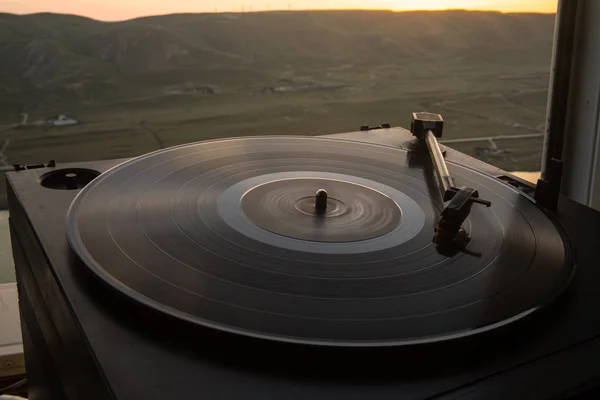 Turntable vinyl record player on the background of a sunset over the mountains. Sound technology for DJ to mix & play music. Black vinyl record. Vintage vinyl record player. Needle on a vinyl record