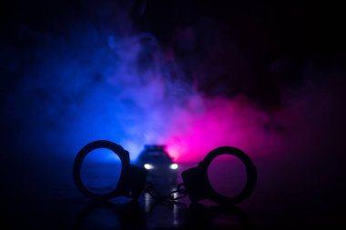 Polis baskını gece ve sen altında tutuklama kavramı vardır. Kelepçe arka polis araba ile silüeti. Görüntü yanıp sönen kırmızı ve mavi polis ışıklardan sisli arka plan ile. Kaymak vurdu