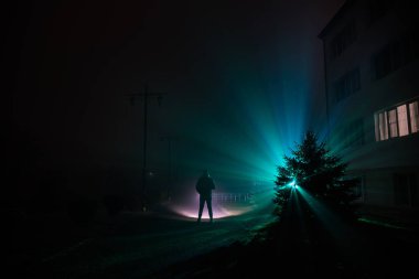 Gece manzarası. Gece yoğun sis içinde şehir. Mistik manzara ürkütücü adam gerçeküstü ışıklarla. Yapay ışıkta gece siste yürüyen adamın siluet. Arka aydınlatma karışık güzel.