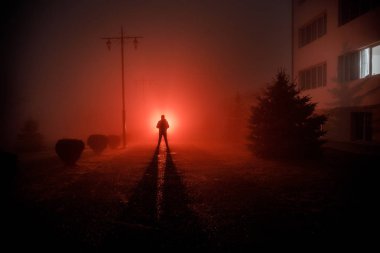 Gece manzarası. Gece yoğun sis içinde şehir. Mistik manzara ürkütücü adam gerçeküstü ışıklarla. Yapay ışıkta gece siste yürüyen adamın siluet. Arka aydınlatma karışık güzel.