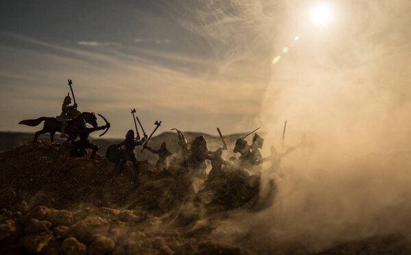 Medieval battle scene with cavalry and infantry. Silhouettes of figures as separate objects, fight between warriors on sunset foggy background. Selective focus