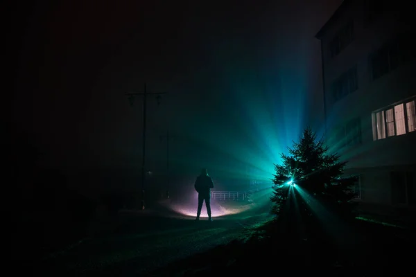 Night Landscape. City at night in dense fog. Mystical landscape surreal lights with creepy man. The walking man's silhouette in night fog at artificial light. Beautiful mixed lighting from backside.