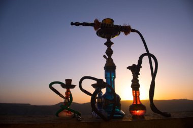 Nargile, geleneksel Arapça harcamak, doğrudan günbatımı güneş ışığı, açık fotoğraf. Dağ arka plan veya nargile günbatımı arka plan üzerinde siluetleri. Açık. Seçici odak
