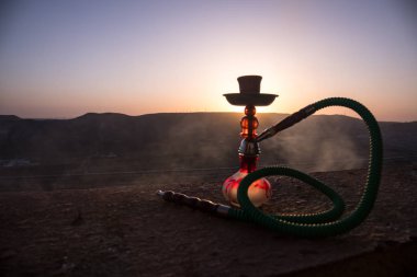 Nargile, geleneksel Arapça harcamak, doğrudan günbatımı güneş ışığı, açık fotoğraf. Dağ arka plan veya nargile günbatımı arka plan üzerinde siluetleri. Açık. Seçici odak