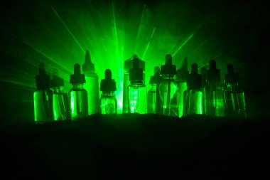 Vape konsepti. Karanlık arka planda duman bulutları ve tüp sıvısı şişeleri. Işık efektleri. Arka plan, vape reklamı ya da vape arkaplan olarak kullanışlı. Seçici odak