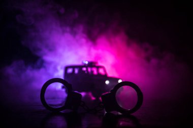 Polis baskını gece ve sen altında tutuklama kavramı vardır. Kelepçe arka polis araba ile silüeti. Görüntü yanıp sönen kırmızı ve mavi polis ışıklardan sisli arka plan ile. Kaymak vurdu
