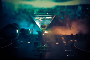 Martini gece kulübünde dj denetleyicisinde içinde zeytin ile bardak. Club içki müzik parti disko ışıkları ile gece kulübünde DJ konsolu.