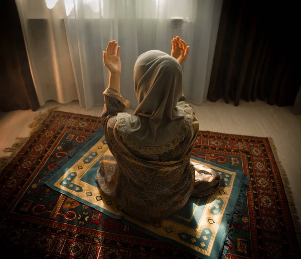 穆斯林妇女在窗口附近的房间祈祷真主的穆斯林上帝 穆斯林妇女的手在地毯上祈祷传统穿着衣服 妇女在头巾 地毯的克尔白 选择性重点 — 图库照片
