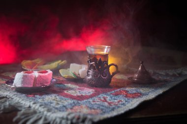 Cam bir halı ile ışık ve duman koyu arka plan üzerinde Doğu snacks ile Arap tea. Doğu çay kavramı. Boş alanı. Seçici odak.