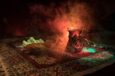 Cam bir halı ile ışık ve duman koyu arka plan üzerinde Doğu snacks ile Arap tea. Doğu çay kavramı. Boş alanı. Seçici odak.