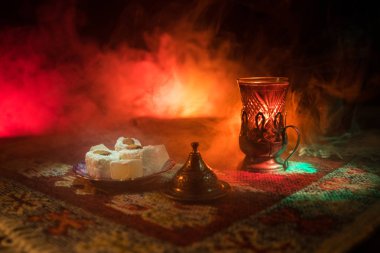 Cam bir halı ile ışık ve duman koyu arka plan üzerinde Doğu snacks ile Arap tea. Doğu çay kavramı. Boş alanı. Seçici odak.
