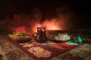Cam bir halı ile ışık ve duman koyu arka plan üzerinde Doğu snacks ile Arap tea. Doğu çay kavramı. Boş alanı. Seçici odak.