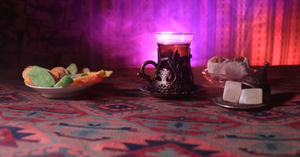 阿拉伯茶在老式玻璃与东方小吃在地毯上 东部茶仪式在黑暗的背景与灯和烟雾 空的空间 选择性对焦 滑块射击 — 图库视频影像