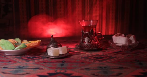阿拉伯茶在老式玻璃与东方小吃在地毯上 东部茶仪式在黑暗的背景与灯和烟雾 空的空间 选择性对焦 滑块射击 — 图库视频影像