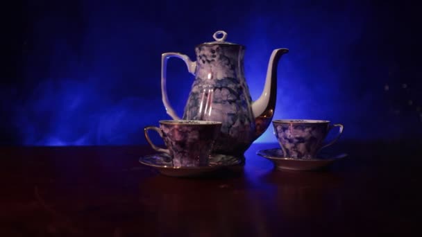 咖啡或茶道的概念主题 老式的陶瓷茶或咖啡壶与杯壶和糖杯在黑暗色调背景与光和烟雾 文本的空白 滑块射击 — 图库视频影像