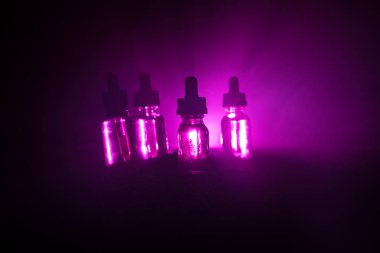 Vape konsepti. Karanlık arka planda duman bulutları ve tüp sıvısı şişeleri. Işık efektleri. Arka plan, vape reklamı ya da vape arkaplan olarak kullanışlı. Seçici odak