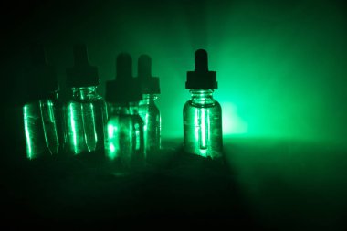Vape konsepti. Karanlık arka planda duman bulutları ve tüp sıvısı şişeleri. Işık efektleri. Arka plan, vape reklamı ya da vape arkaplan olarak kullanışlı. Seçici odak