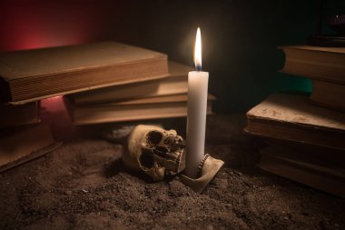 Büyücünün Resepsiyon. Bir resepsiyon tarafından mum ışığı yaktı. Bir insan kafatası, kum yüzeyi eski kitaplar. Cadılar Bayramı natürmort arka plan koyu tonda sisli arka plan üzerinde farklı bir eleman ile. Seçici odak