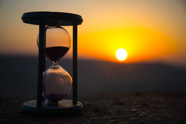 Hourglass Passing of Time Lapse Clouds. An hourglass in front of a bright blue sky with puffy white clouds passing. Time concept. Sunset time. Selective focus
