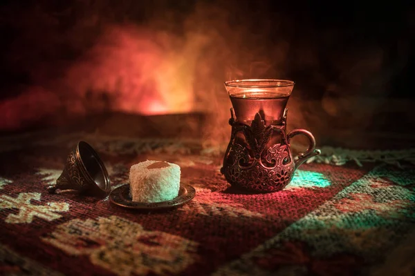Cam bir halı ile ışık ve duman koyu arka plan üzerinde Doğu snacks ile Arap tea. Doğu çay kavramı. Boş alanı. Seçici odak.