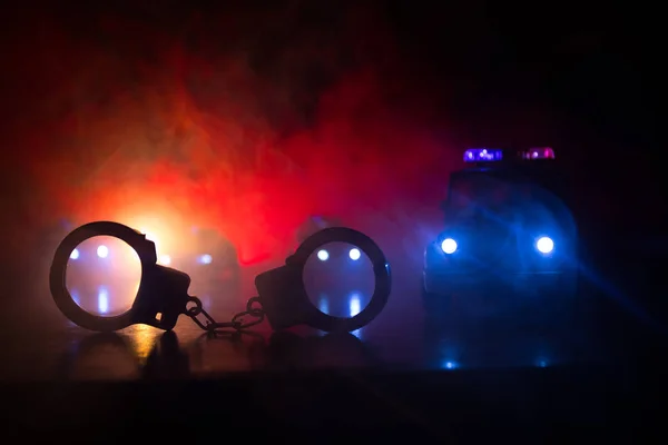 警方在夜间突袭 你被逮捕的概念 背后有警车的手铐剪影 图像与闪烁的红色和蓝色的警察灯在雾的背景 滑块射击 — 图库照片