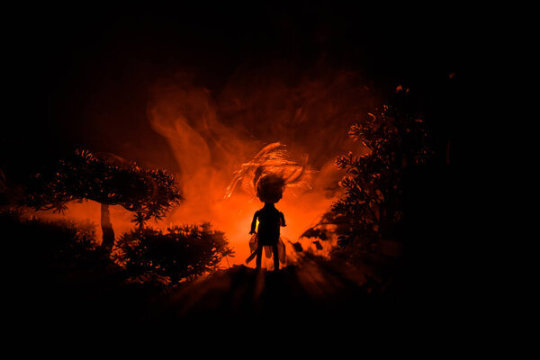 Horror Halloween decorated conceptual image. Alone girl with the light in the forest at night. Silhouette of girl standing between trees with surreal light on background. Selective focus.