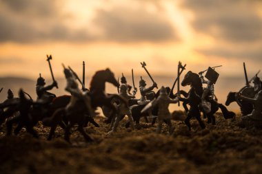 Medieval battle scene with cavalry and infantry. Silhouettes of figures as separate objects, fight between warriors on sunset foggy background. Selective focus clipart