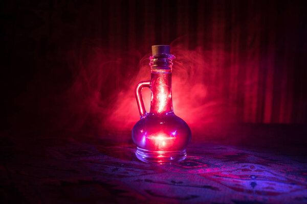 Antique and vintage glass bottle on dark foggy background with light. Poison or magic liquid concept.