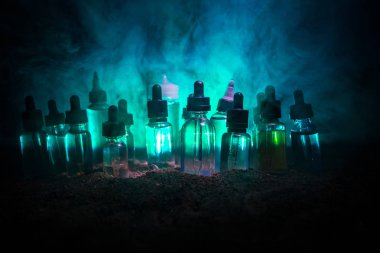 Vape konsepti. Karanlık arka planda duman bulutları ve tüp sıvısı şişeleri. Işık efektleri. Arka plan, vape reklamı ya da vape arkaplan olarak kullanışlı. Seçici odak