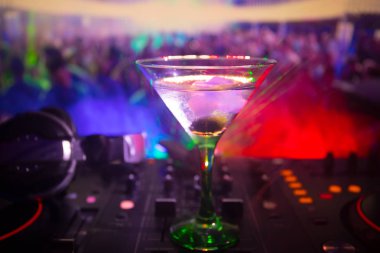 Martini gece kulübünde dj denetleyicisinde içinde zeytin ile bardak. Club içki müzik parti disko ışıkları ile gece kulübünde DJ konsolu.