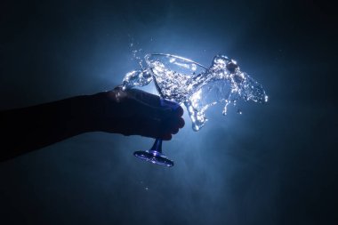 Martini kokteyl cam el koyu tonda dumanlı arka plan veya renkli kokteyl cam su sıçramalarına ve zeytin sıçramasına. Parti club eğlence. Karışık ışık. Seçici odak