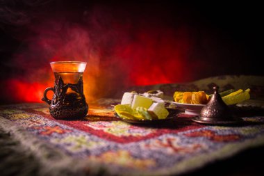 Cam bir halı ile ışık ve duman koyu arka plan üzerinde Doğu snacks ile Arap tea. Doğu çay kavramı. Boş alanı. Seçici odak.
