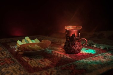Cam bir halı ile ışık ve duman koyu arka plan üzerinde Doğu snacks ile Arap tea. Doğu çay kavramı. Boş alanı. Seçici odak.